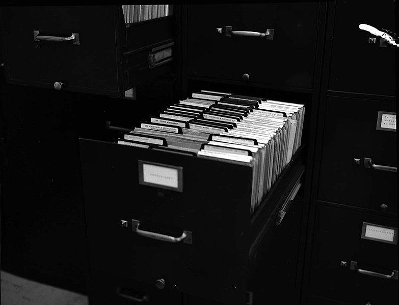 A black and white photo of a filing cabinet with an open drawer showcasing many tabbed dividers